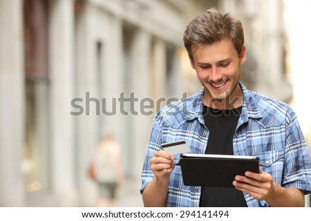 Young man buying online with a credit card and a tablet in the street