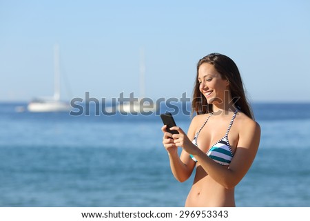 Sunbather girl wearing bikini using a smart phone on summer holidays on the beach