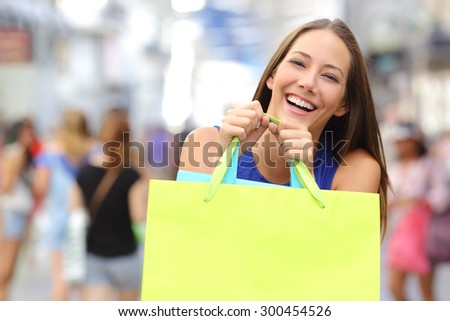 Shopper girl buying in a mall and holding a green shopping bag smiling to the camera