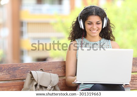 Freelancer working with a laptop and headphones sitting on a bench in a park