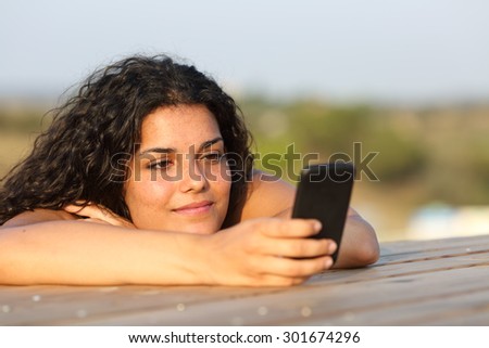 Relaxed girl watching social media in a smart phone in a park or home table with the sky in the background