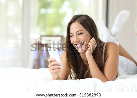 Happy girl using a mobile phone lying on the bed at home