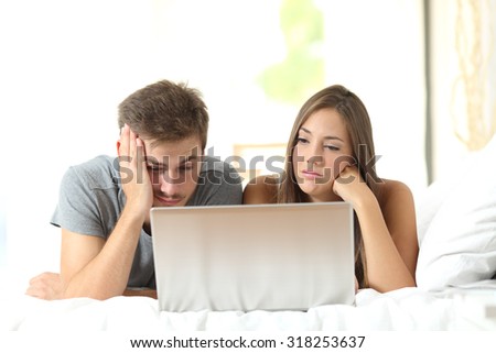 Bored marriage watching media in a laptop lying on a bed at home