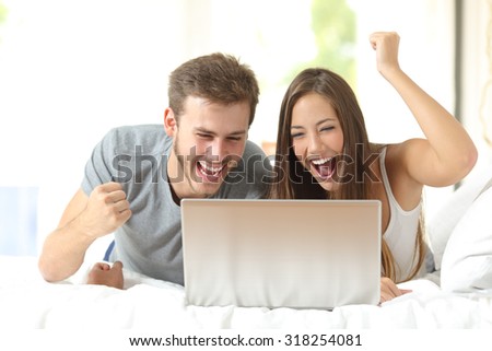Euphoric marriage winning using a laptop lying on a bed at home