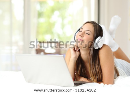 Girl feeling and listening to the music with headphones and laptop on the bed at home