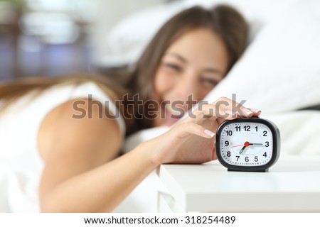 Happy girl waking up in the morning turning off the alarm clock in her bedroom