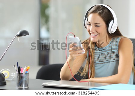Girl listening to the music with a smartphone and headphones in her desktop at home