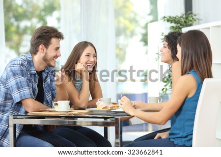 Group of 4 happy friends meeting and talking and eating desserts on a table at home