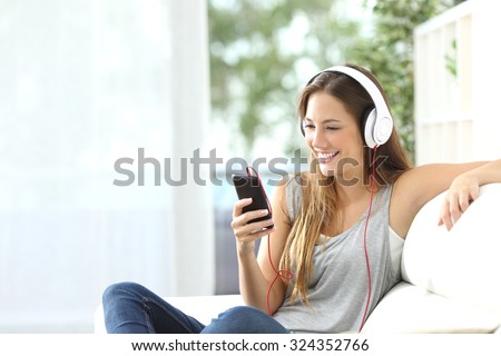Happy girl listening to music from mobile phone sitting on a couch at home