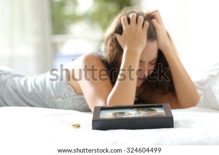Sad wife missing her husband after divorce with a broken picture of the couple and a engagement ring in the foreground