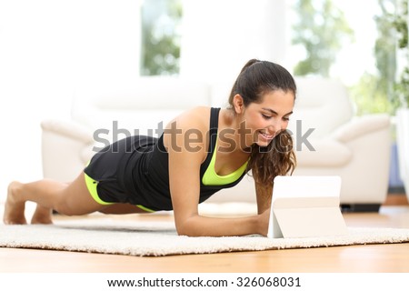 Fitness woman exercising on the floor at home and watching fitness videos in a tablet