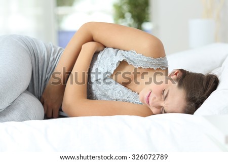 Girl suffering menstrual pains lying on the bed at home