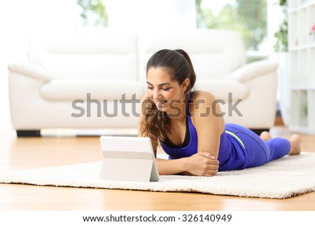 Sportswoman watching sport videos in a tablet lying on the floor at home