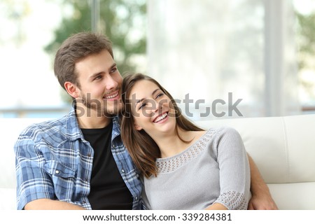 Happy couple thinking and looking sideways sitting on a couch at home