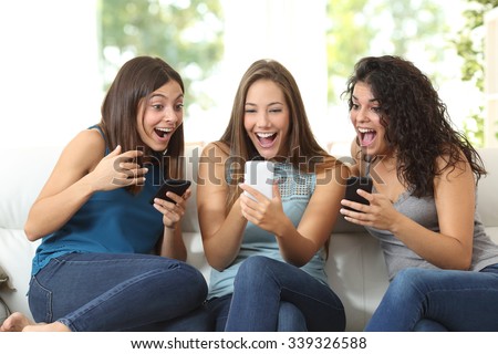 Three friends amazed watching a smart phone sitting on a couch at home