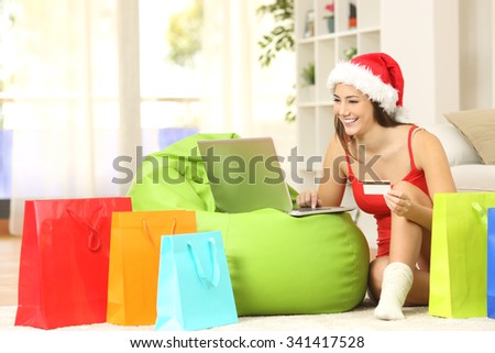 Casual girl buying online for christmas sitting on the floor with colorful shopping bags at home