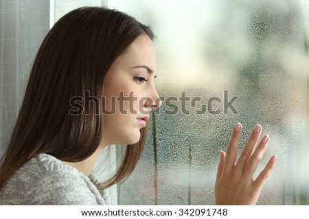 Sad woman looking the rain falling through a window at home or hotel