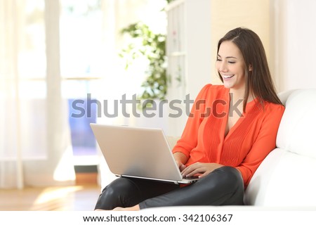 Entrepreneur woman wearing orange blouse working with a laptop sitting on a couch at home