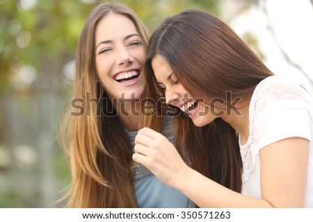 Two happy woman friends laughing together in a park with a green background