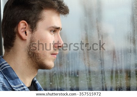 Side view of a man longing and looking through window in a sad rainy day