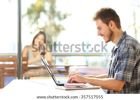 Side view portrait of a student learning on line and typing in a laptop sitting in a coffee shop