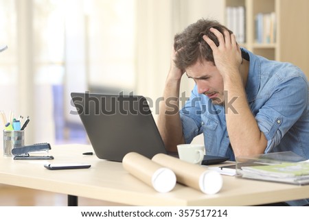Sad freelance male worried watching bad news on line with a laptop on a desk at home or a little office