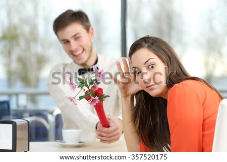 Disgusted woman rejecting a geek boy offering flowers in a blind date in a coffee shop interior