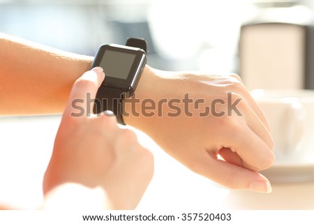 Close up of a female hands using a generic modern smart watch on line pushing a button and showing the blank screen in a bar terrace in a sunny day