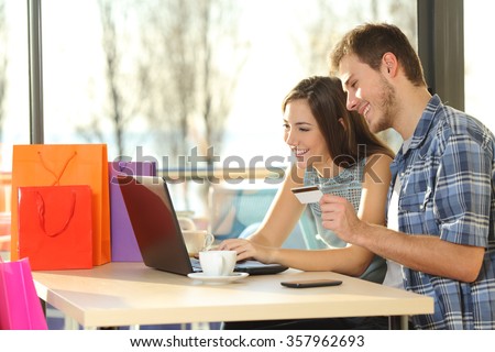 Couple buying online with credit card and laptop with shopping bags in a coffee shop