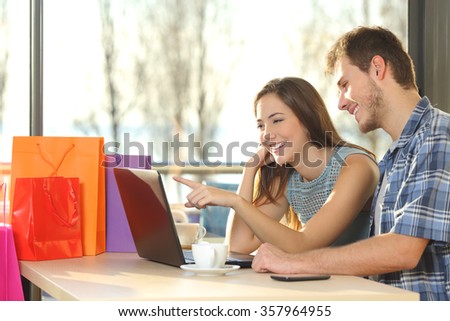 Couple of shoppers with shopping bags buying online and choosing products in a coffee shop
