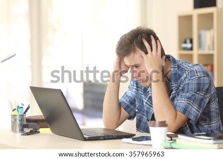 Worried and sad student male watching exam results on line in a laptop in a desk sitting at home room