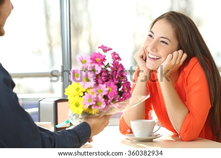 Candid woman dating in a coffee shop and looking her boyfriend who gives her a bunch of flowers