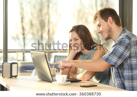 Profile of a happy couple searching information on line together connected in a laptop inside a coffee shop with an exterior background