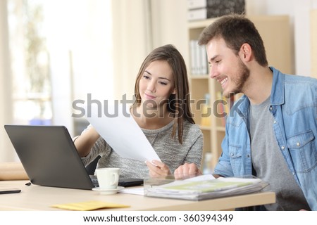 Two entrepreneurs sitting together working in an office desk comparing documents
