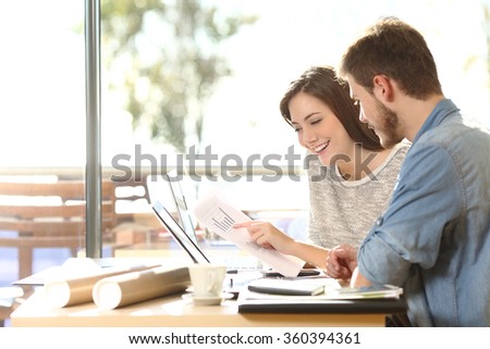 Group of two coworkers working comparing forecasting graphics in a coffee shop with a window in the background