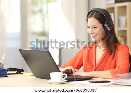 Beautiful freelancer female talking in a video conference on line with a headset with microphone and laptop in an office desktop or home desk