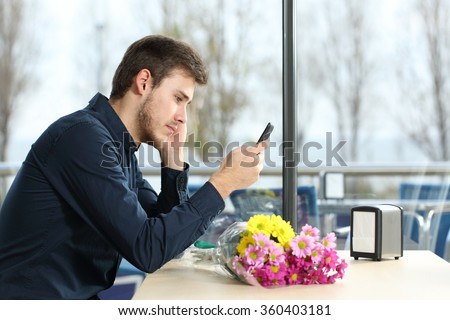 Sad man with a bouquet of flowers stood up in a date checking phone messages in a coffee shop