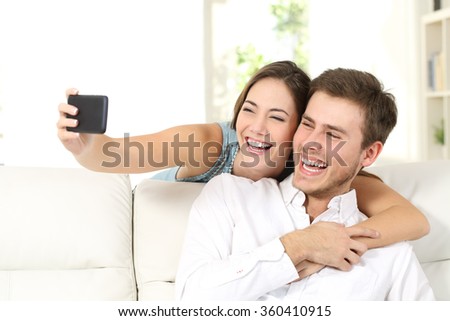 Marriage or couple laughing and taking a selfie with phone sitting on a couch at home