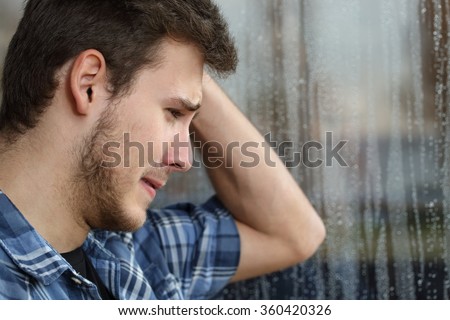 Side view of a sad man looking through window almost crying in a rainy day