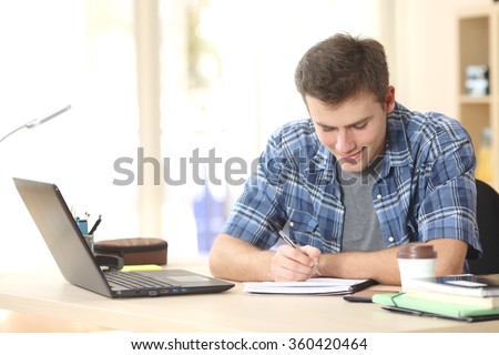 Student studying and writing notes in a notebook sitting at a desk at home