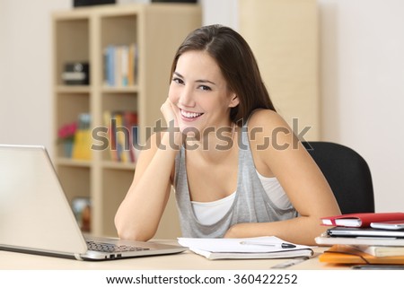 Happy student smiling posing looking at camera sitting on a chair in a desk at home
