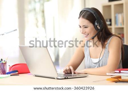 Student talking in a video call on line with headsets and a laptop in a desk at home
