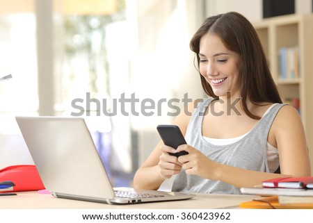 Beautiful relaxed student learning with laptop and texting in a mobile phone in a desk at home