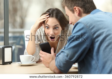 Surprised couple meeting in a coffee shop watching media content in a smart phone