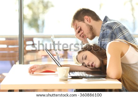 Side view of tired students surrendering to fatigue studying with laptops in a coffee shop with a window in the background and sky outdoors
