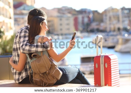 Couple of tourists sitting searching information or booking an hotel on a smart phone on vacations in a colorful port promenade