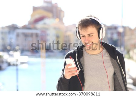 Front view of a teenager walking towards camera listening music with headphones from smart phone in a vacations destination