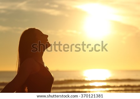 Side view of back light of a woman silhouette breathing deep fresh air at warm sunrise in front of sun