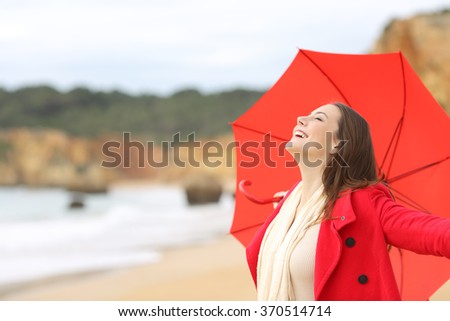 Joyful woman wearing red jacket breathing fresh air excited with an umbrella on the beach