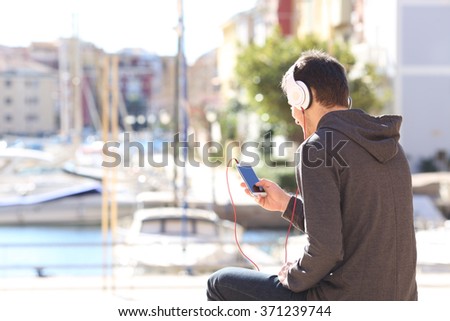 Back view of a teenager listening music with headphones from a smart phone on a vacations destination